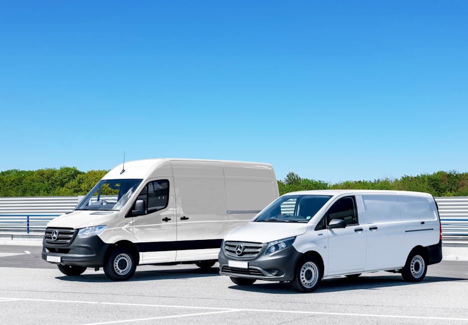 A row of five white and gray removal vans parked closely together on a paved surface, with their rear doors facing the camera. Each van has a yellow UK registration plate and tinted rear windows, some